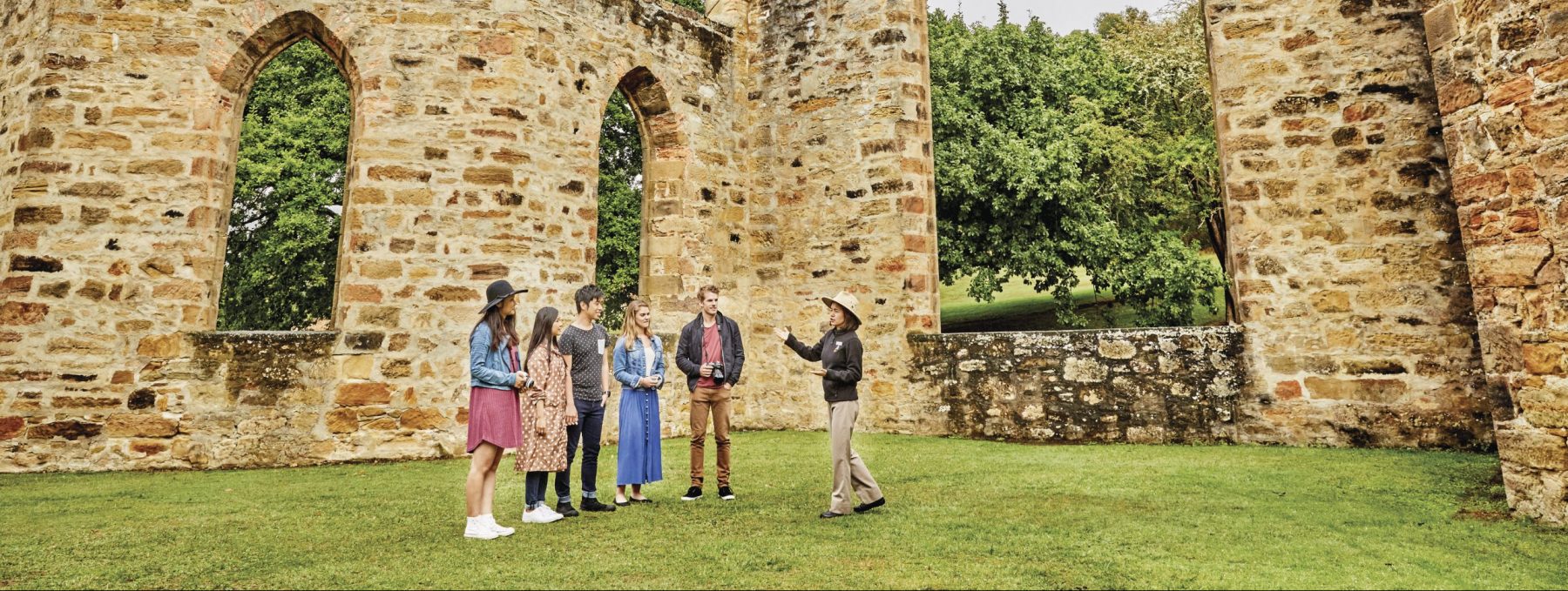 a port arthur guide in uniform speaking to a group of visitors in the sandstone ruins of the Convict Church