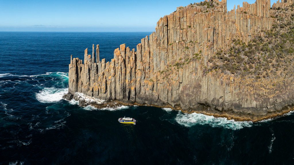 aerial image of the Cape Raoul Cruises vessel beneath the towering dolerite cliffs of Cape Raoul