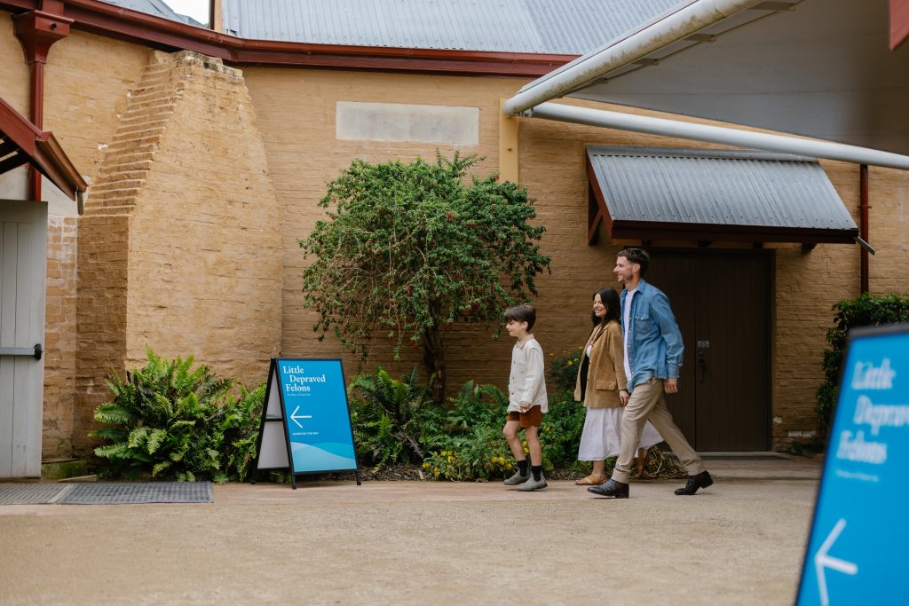 Two adults and a child walking into a building with a sign outside reading, 'Little Depraved Felons'