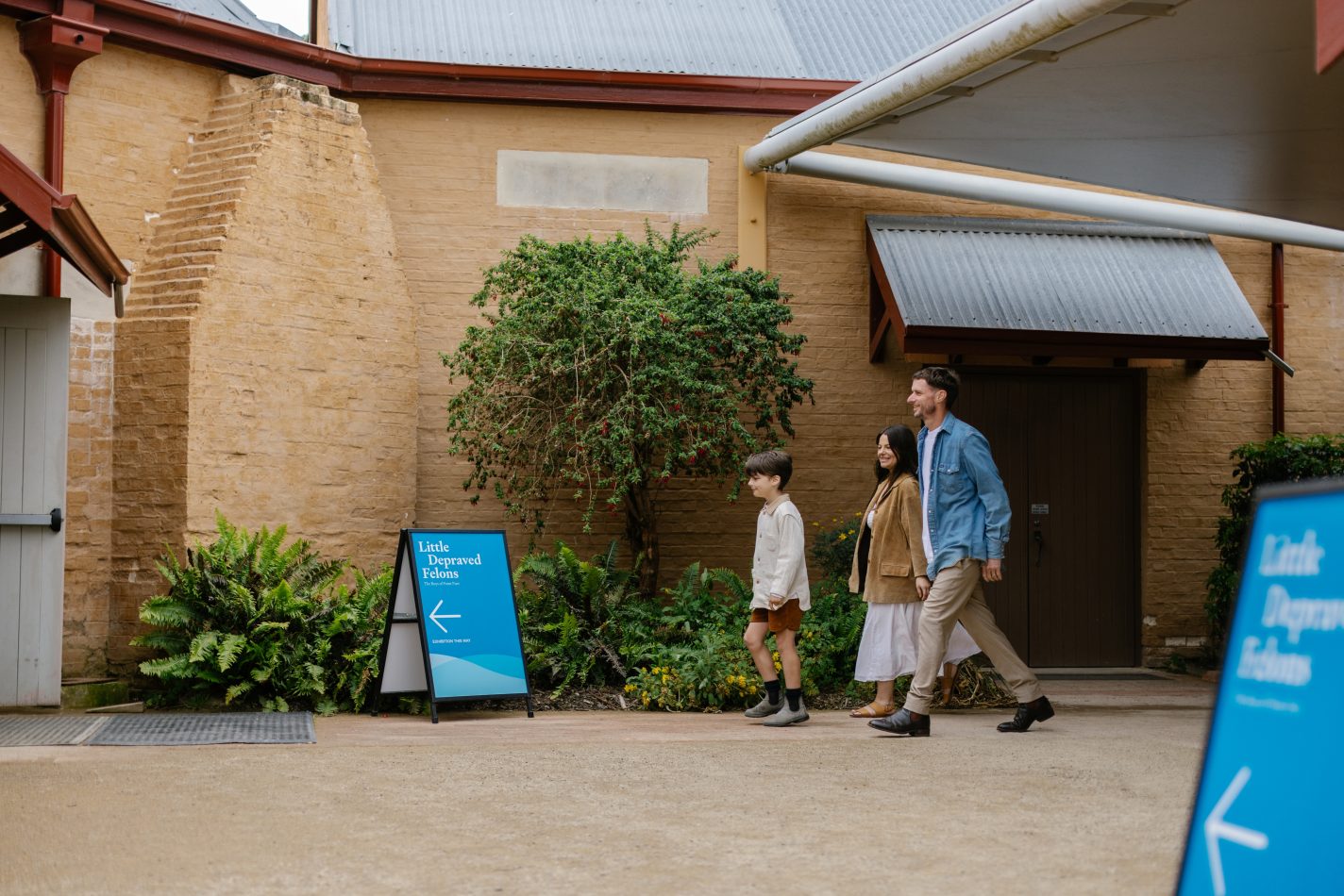 Two adults and a child walking into a building with a sign outside reading, 'Little Depraved Felons'